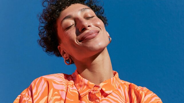 Close-up portrait of a young woman with curly hair. she is wearing an orange blouse with a zigzag pattern and large hoop earrings.