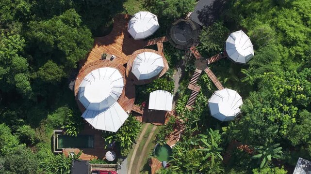 Aerial drone footage captures a stunning villa in Costa Rica featuring white geodesic dome structures connected by wooden decks nestled within lush tropical rainforest with pool and greenery.