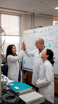 Research team celebrating a breakthrough at a whiteboard in a science laboratory