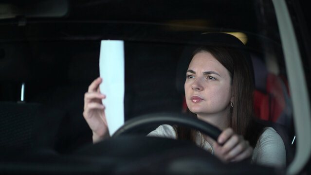 A young woman in the driver's seat holds a white paper receipt and looks at it seriously with a concerned expression, hand on the steering wheel.