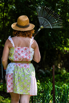 Woman gardener with straw hat carrying a rake in a vegetable garden