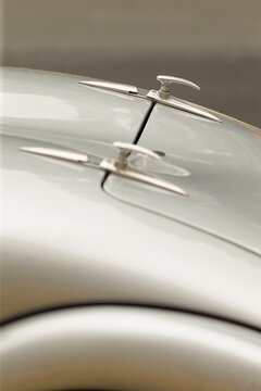 Tight detail of a classic automobile hood showing three polished chrome hood ornaments mounted along a pale metallic surface. Soft studio lighting highlights