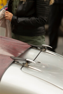 Tight view of a classic car hood showing a leather tonneau cover secured by polished chrome latches and fasteners. Soft reflections appear on the