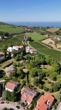 Aerial drone view of Roseto degli Abruzzi town residential houses with solar panels near green vineyards and hills by Adriatic sea coast in Italy.