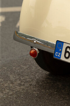 Close-up view of the rear corner of a cream-colored vintage car showing a chrome bumper, round red taillight, and a partial European license plate mounted on