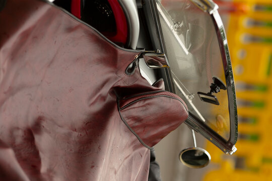 Close-up view of a retro scooter showing a maroon leather leg cover draped over the front apron, chrome windscreen frame and small round mirror. Soft studio