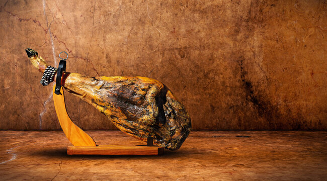  Jam&oacute;n ib&eacute;rico sobre soporte fondo marr&oacute;n grunge r&uacute;stico. Pierna de jam&oacute;n curada sobre fondo r&uacute;stico. Sugiere tradici&oacute;n, calidad artesanal y patrimonio culinario espa&ntilde;ol.