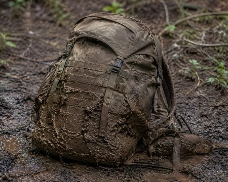 Thick Mud Coating Lower Half Of Rugged Hiking Backpack Dumped On Ground After Wilderness Adventure
