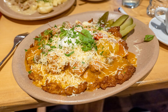 Large portion of Polish potato pancakes with meat sauce, grated cheese and sour cream, served with pickles and microgreens on ceramic plate at restaurant table, rustic European comfort food, no people