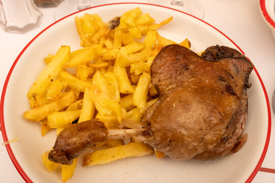 Perfectly cooked duck leg confit de canard with crispy golden skin and tender meat, served with golden French fries at authentic Parisian caf&eacute; bistro, paired with a glass of wine