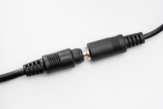 Black DC barrel power connectors joined on white background, closeup of male and female adapter cable coupler, low voltage electronics repair, extension lead and power supply safety concept, no people