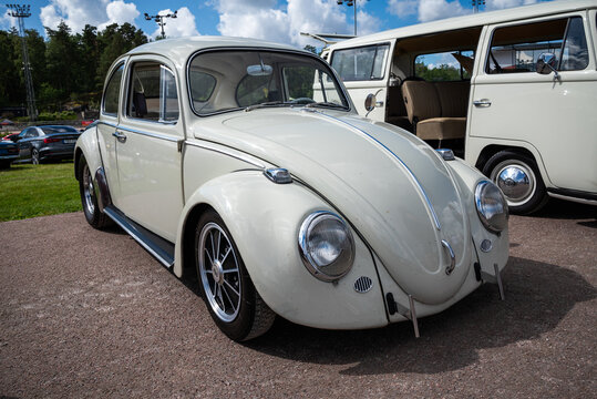 Stockholm, Sweden - August 2, 2025: Cream classic Volkswagen Beetle with chrome bumpers and alloy wheels beside a VW Bus at Stockholm Car Meet