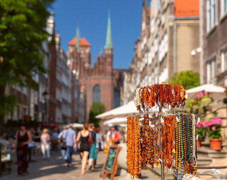 Display of handmade amber jewelry on a historic street in the Old Town of Gdansk, Poland, with St. Mary's Church visible in the background.