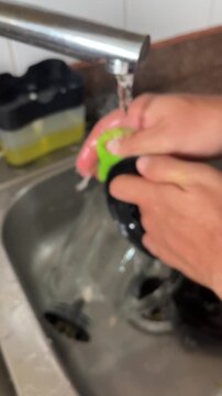 Young man washing blender part under running water in kitchen sink