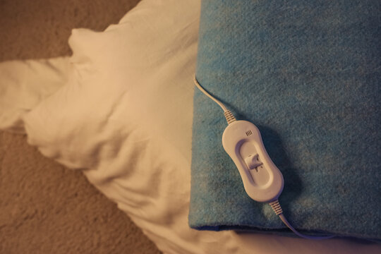 Folded electric heating pad with controller on bed in room at night, top view