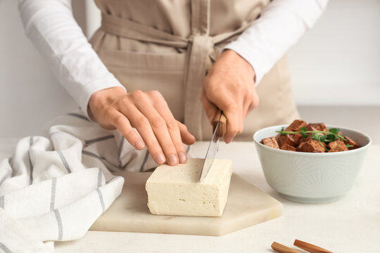 Woman cutting tofu cheese on white table