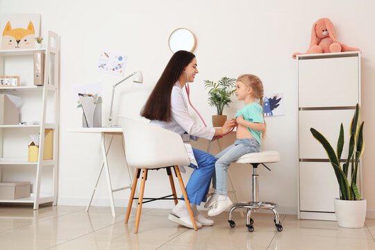 Female pediatrician with stethoscope listening to little girl in clinic