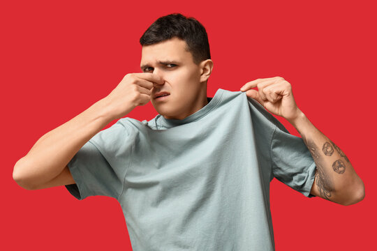 Handsome young man feeling bad smell from dirty clothes on red background