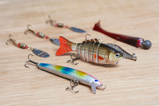 Assorted fishing lures including jointed swimbait, minnow plug, spinner and soft plastic bait on wooden surface. Predator fishing tackle for freshwater angling, outdoor, sport fishing and camping.