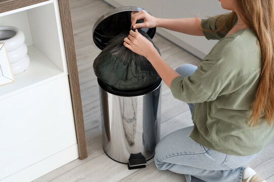 Woman throwing full garbage bug into trash bin in kitchen