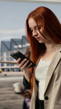 Vertical frame: Woman in airport photographs plane ticket with smartphone, passenger takes picture of flight information on boarding pass before departure using phone camera, keeping digital copy.