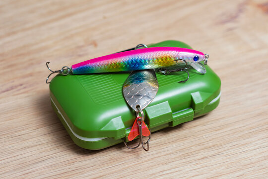 Fishing tackle box with minnow lure and metal spinner on wooden surface. Artificial baits for predator fishing, freshwater angling, tackle retail, outdoor recreation and sport fishing equipment.
