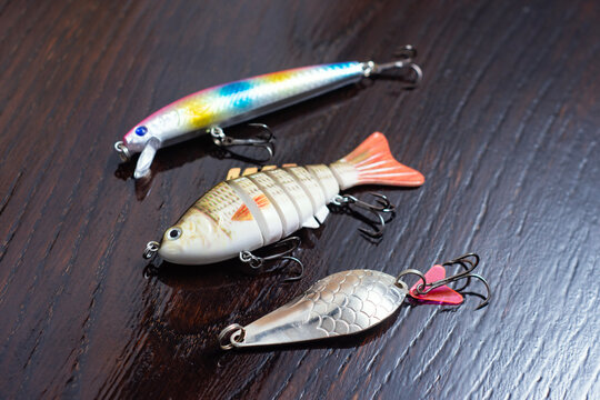 Artificial fishing lures assortment with hard plastic wobbler, multi jointed swimbait and metal spoon on dark wooden background. Angling gear, predator fish tackles or sport fishing retail concept.