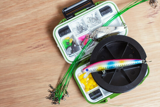 Fishing tackle box with braided fishing line, minnow lure, wire leaders and terminal tackle on wooden surface. Freshwater angling equipment for sport fishing, outdoor retail and camping.