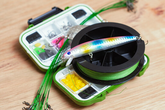 Fishing tackle box with braided fishing line, minnow lure, wire leaders and terminal tackle on wooden surface. Freshwater angling equipment for sport fishing, outdoor retail and camping.