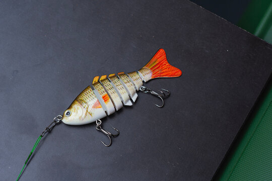 Jointed swimbait fishing lure with treble hooks and wire leader on dark background. Artificial bait for predator fishing, freshwater angling, tackle advertising, outdoor retail and sport fishing.