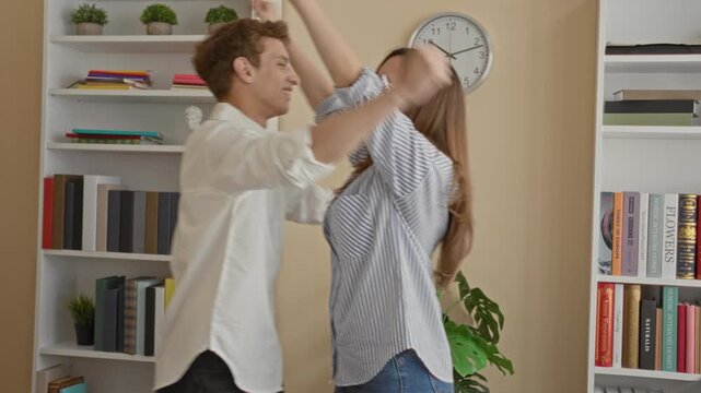Man and woman embrace with arms around back and bookshelf and wall clock visible in building; reunion comfort.