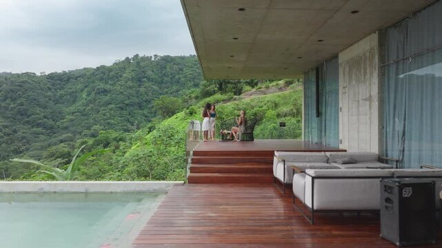 Three close friends are relaxing by a stunning pool at a beautiful Costa Rican house surrounded by lush greenery and sleek modern architecture, enhancing the scenery and vibe