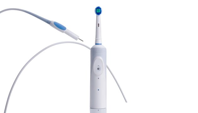 A white electric toothbrush, and a dental tool are arranged against a stark, white background, creating a clean composition