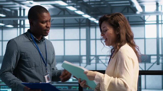 System administrators use documents in a server room to review technical files and confirm a client agreement, combining client agreement, technical meeting and business deal.