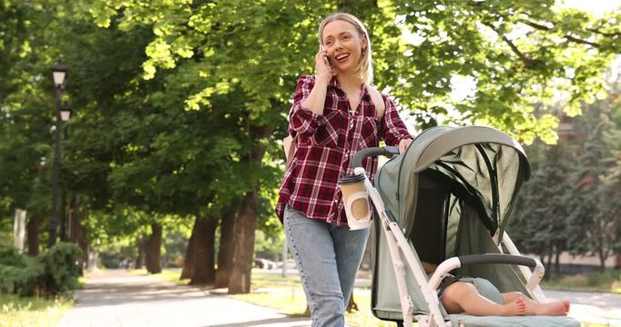 Baby carriage. Mother talking on smartphone while walking with her child in stroller outdoors