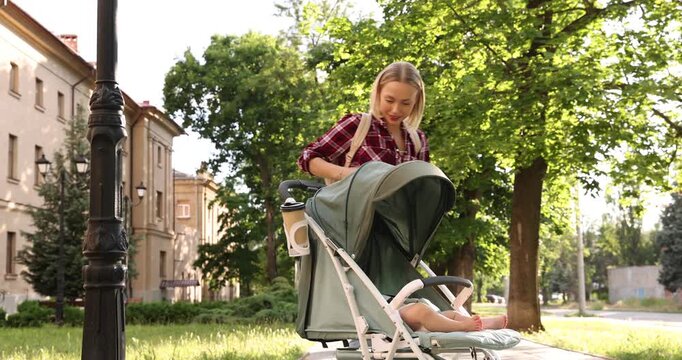 Baby carriage. Mother talking on smartphone while walking with her child in stroller outdoors, low angle view