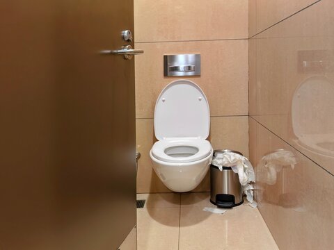 The toilet with a white sitting closet and a trash can seemed to be full of stacked tissues.