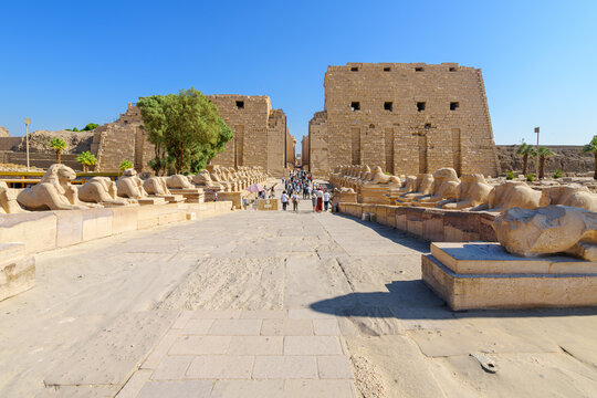 Tourists on The Way of the Rams featuring ram headed sphinxes lined on both sides as they approach the First Pylon of the Karnak Temple Complex in Luxor Egypt.