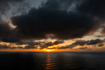 Fototapeta premium Dramatic sunset over the dark ocean with heavy clouds and golden light reflection