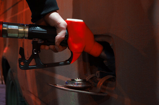 Night street city photo. Man fills car with gasoline. Male hand holds red petrol gun, fuel dispenser, petroleum dispensing nozzle on gas station. Concept of crisis in Russia, rising oil prices, sale
