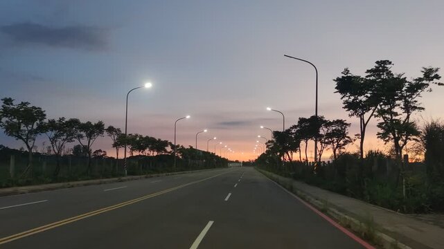 The beautiful scenery of straight roads bathed in the glow of the setting sun, illuminated by streetlights.