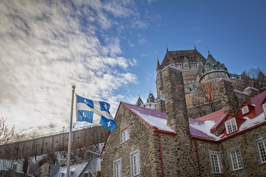 Quebec flag with fleur-de-lys and white cross waving in winter near Chateau de Frontenac, with Old Quebec stone buildings, snowy rooftops and provincial heritage scenery.