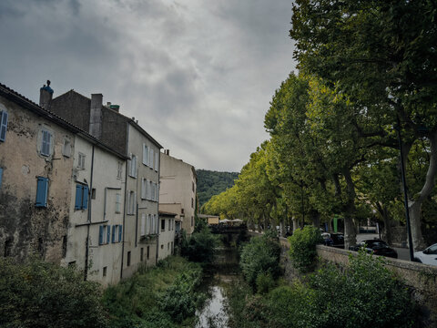 Panoramic view of the Collobrieres village center with old houses, shutters, a small river, tree-lined street and wooded hills in Provence, southern France, showing a typical inland Var settlement.