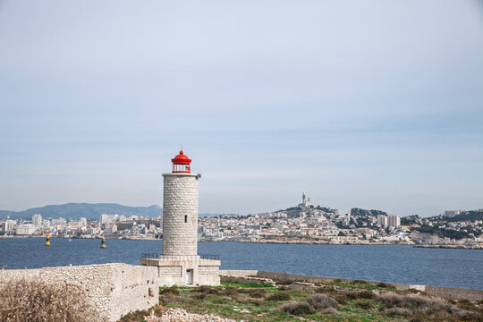 Panorama of Marseille with Notre Dame de la Garde, or Bonne Mere, seen across the mediterranean sea from a lighthouse viewpoint with rocky foreground and harbor markers in France on iles du frioul.