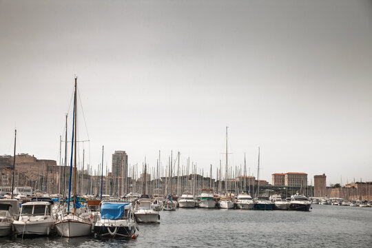 Panoramic view of Vieux Port in Marseille, France, showing boats and sailboat masts in the historic harbor, waterfront buildings, city skyline and Mediterranean marina scenery in france.
