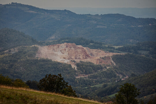 Large open-pit mine or stone quarry in forested hills, showing exposed rock, excavation terraces, access roads, and the impact of resource extraction on the landscape in Serbia.