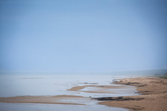 Panoramic view of Garciems beach, also called Garciema Pludmale, with wet sand, mist, calm Baltic Sea water and a foggy, cloudy sky at the Latvian coastal resort in Latvia.
