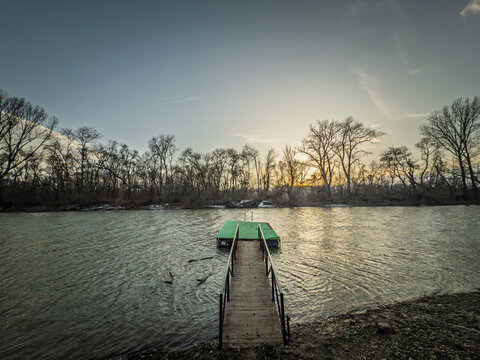 A small pontoon extends onto the Timis or Tamis River in Glogonj, Vojvodina, Serbia, with bare riverside trees, calm water and sunset light creating a quiet nature scene.