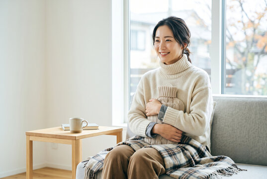 ソファで湯たんぽを抱え暖まる笑顔の女性