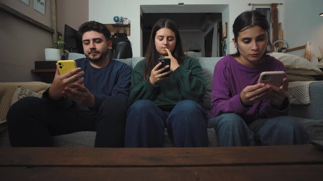 Group of young Hispanic friends sitting on a sofa in a messy apartment, each focused on their own smartphone instead of interacting, highlighting digital distraction, social disconnection, and everyda